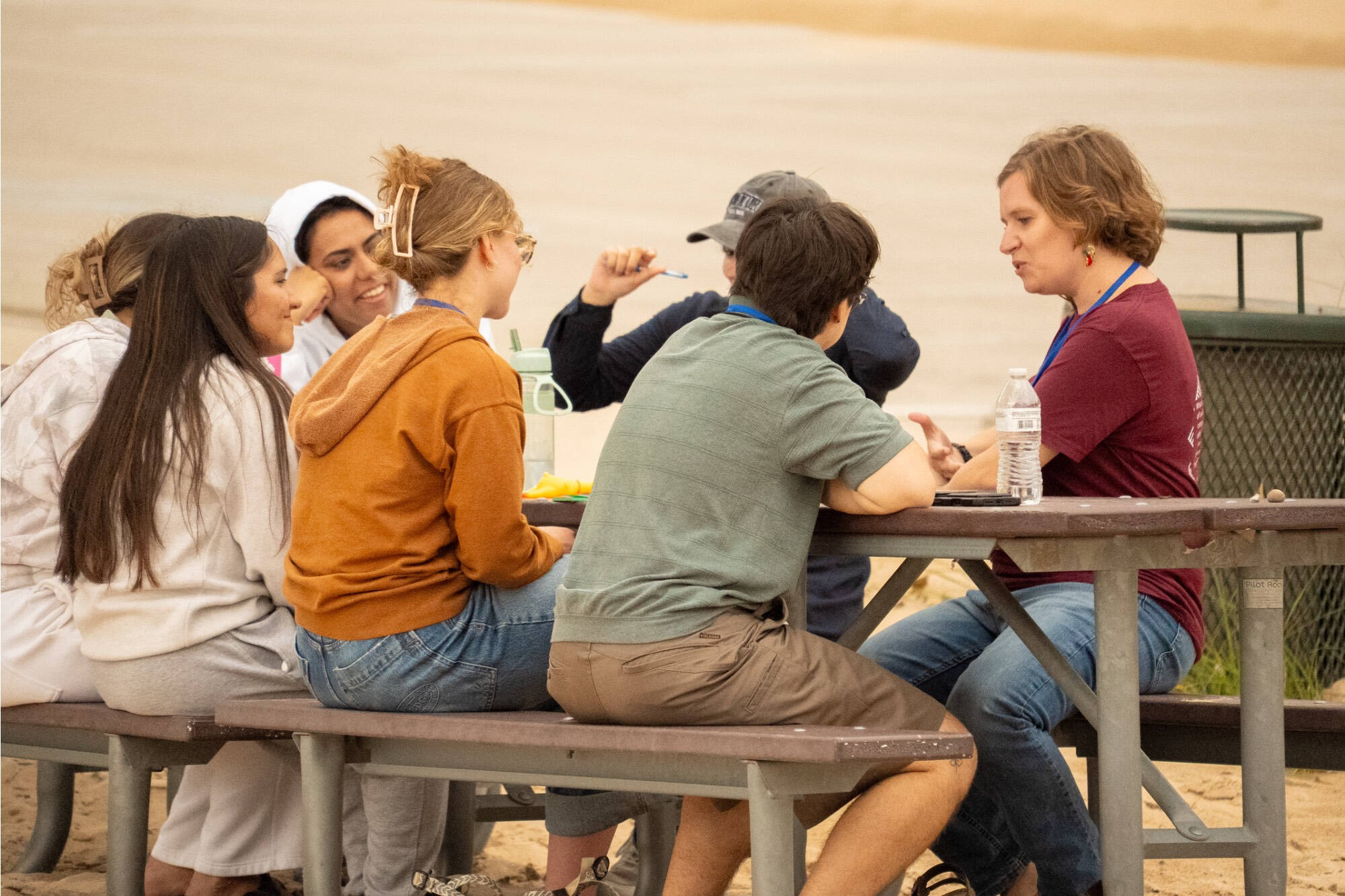 A group of people at a picnic table on the beach chatting and smiling.